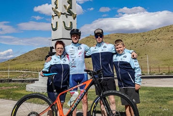 Vier Personen posieren mit einem Mountainbike vor einem hohen Denkmal.
