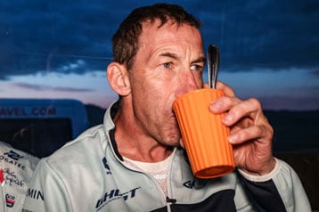 Mann trinkt aus einer orangefarbenen Tasse mit einem Löffel darin.