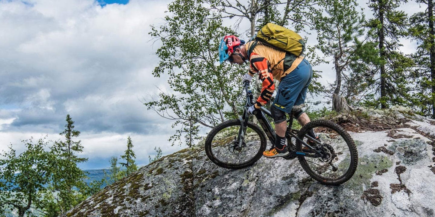 Mountain biker navigating rocky terrain in a forested area under cloudy skies