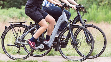 Two people riding electric bicycles on a path in a park