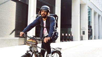 Man riding a bike wearing a helmet and a backpack in an urban area