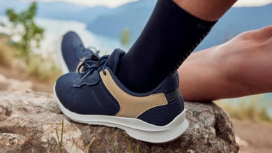 Person wearing navy and beige hiking shoes resting on a rock with scenic mountain background