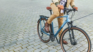 Person riding a blue bicycle on a cobblestone path