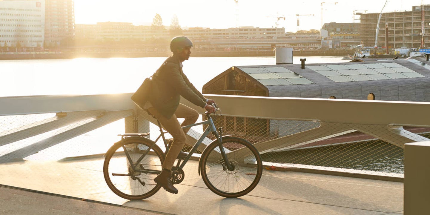 Person cycling on a bridge over a river near a construction site during sunset