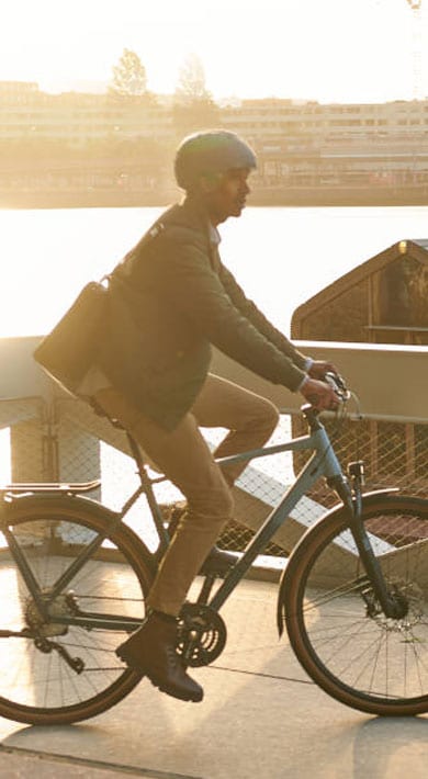 Person cycling on a bridge over a river near a construction site during sunset