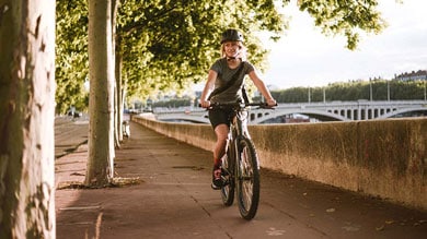 A person biking along a tree-lined pathway near a river