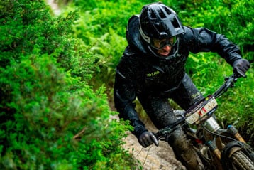 Mountain biker in black gear riding through a muddy forest trail