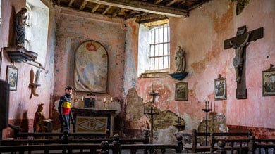 Persoon staat in een oude kerk met religieuze beelden en schilderijen aan de muren.