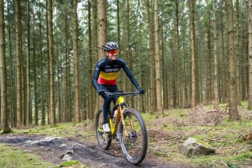 Fietser rijdt over een bospad, met helm en kleurrijk shirt.