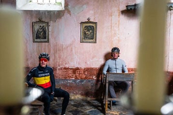 Twee fietsers zitten in een oude kamer met religieuze schilderijen aan de muur.