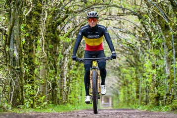 Fietser rijdt over een bospad onder groene bladerbogen.