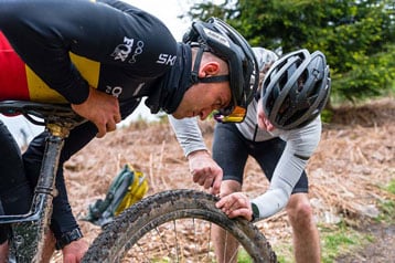 Twee fietsers bekijken een mountainbikewiel op een bospad.