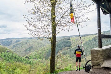 Fietser kijkt uit over een bosrijke vallei met een vlag.