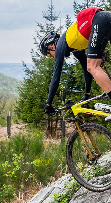 Mountainbiker rijdt een steile rotsachtige helling af in een bosgebied.