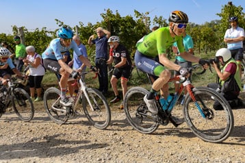 Ciclistas pedalando em uma trilha de gravel com espectadores e fotógrafos