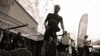 Radfahrer steht mit dem Fahrrad unter einem bewölkten Himmel in der Nähe eines Gebäudes und einer Fahne.