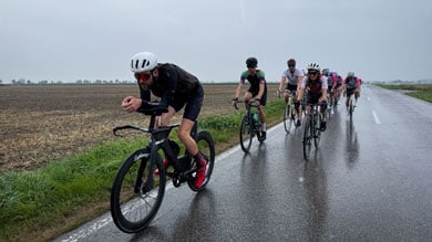 Radfahrer fahren auf einer nassen Landstraße bei bedecktem Wetter.