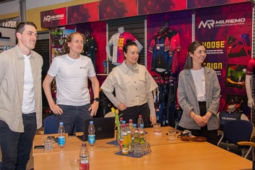 Vier Personen stehen an einem Tisch mit einer Ausstellung von Fahrradbekleidung.