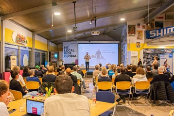 Redner präsentiert einem Publikum in einem hellen Saal mit Radsportdekoration.