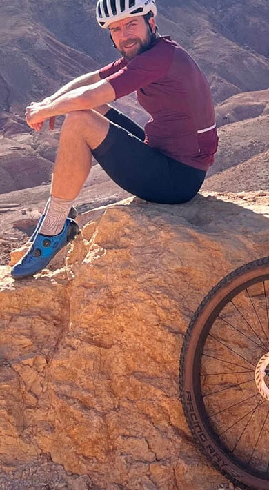 Radfahrer sitzt auf einem Felsen mit einem Fahrrad und blickt auf eine felsige Landschaft.