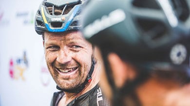Lachender Radfahrer mit Helm, bedeckt mit Schlamm, spricht mit einem anderen Radfahrer