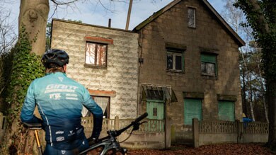Fietser voor een oud, rustiek huis omringd door bomen.