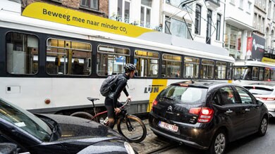 Fietser laveert door verkeer tussen tram en auto's in een stadsstraat.