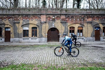 Fietsers rijden langs een oud bakstenen gebouw met bogen.