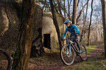 Fietser rijdt op een pad door een bosgebied naast een oude stenen structuur.