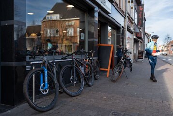 Fietsen geparkeerd buiten een café, persoon in fietskleding met een drankje.