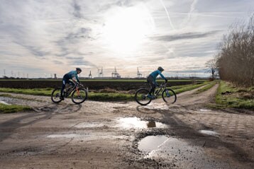 Twee fietsers rijden op een landelijk pad onder een bewolkte hemel.