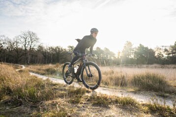Persoon fietst op een pad in een schilderachtig landschap bij zonsondergang.