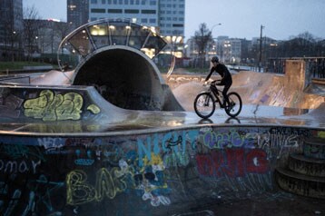 Persoon fietst op een met graffiti bedekte skateparkramp in de schemering.