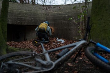 Persoon met rugzak verkent een betonnen structuur, fiets op de voorgrond.