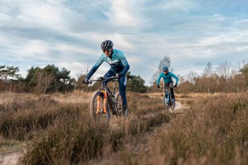 Twee fietsers rijden op mountainbikes over een onverhard pad in de natuur.