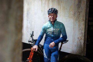 Fietser in blauw tenue en helm staat met een mountainbike binnenshuis.