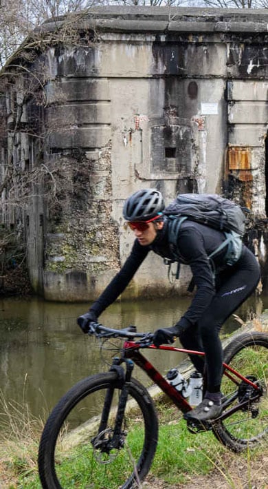 Fietsers rijden langs een oud bakstenen fort in een bosrijk gebied.