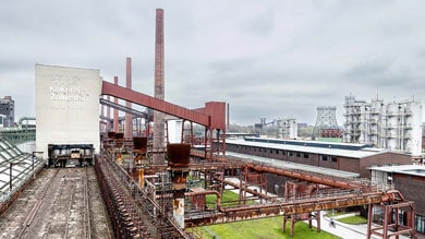 Industrieterrein met rode pijpen en schoorstenen onder een bewolkte hemel.