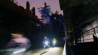 Vervaagde fietsers 's nachts bij een verlicht industrieel bouwwerk.