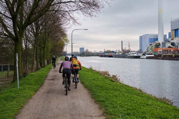 Fietsers op een pad langs de rivier naast een industriegebied.