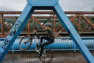Fietser maakt een wheelie op een brug met graffiti.