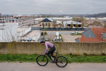 Fietser rijdt bergopwaarts nabij een industriegebied onder een bewolkte lucht.