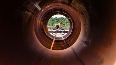 Fietser gezien door een grote metalen buis met bomen op de achtergrond.