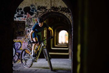 Fietser rijdt door een tunnel vol graffiti.