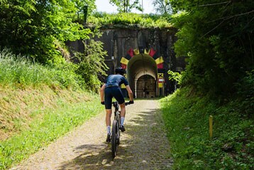 Fietser rijdt richting een tunnelingang omgeven door groen.