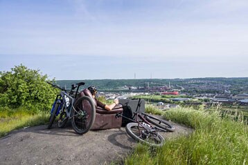 Persoon op een bank met fietsen op een heuvel met uitzicht op een stadsgezicht.