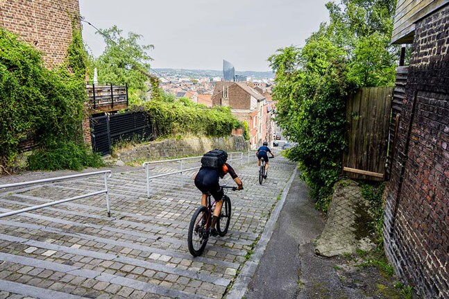 Fietsers rijden een steile straat met kasseien af met uitzicht op de stad op de achtergrond.