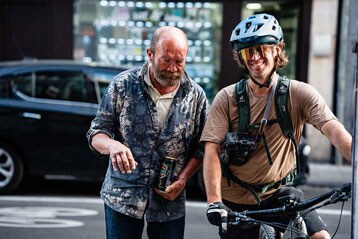 Man met drankje en fietser met helm lachen buiten.