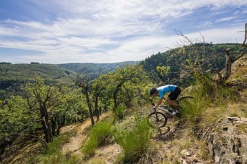 Mountainbiker rijdt over een bospad met een schilderachtig landschap op de achtergrond.