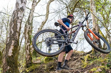 Mountainbiker draagt zijn fiets omhoog op een bospad.